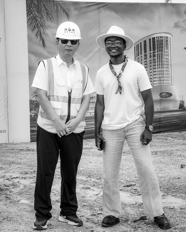 Chimezie Ikenga with a man in a white hard hat in front of the Tri-Tower render on the site hoarding