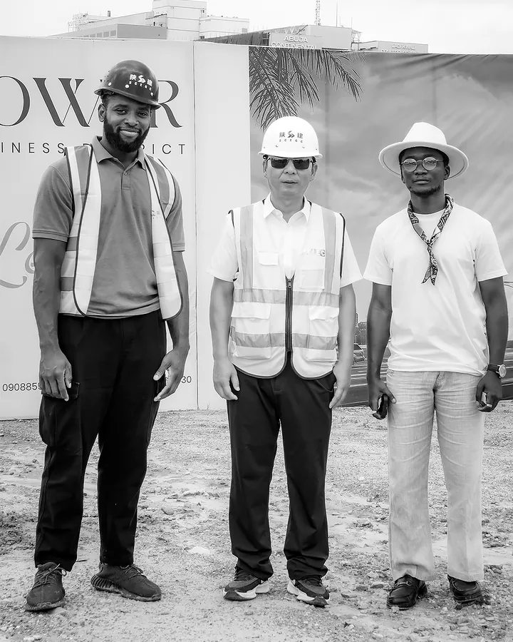 Chimezie Ikenga standing with two men in hard hats and safety vests in front of the Tri-Tower site hoarding