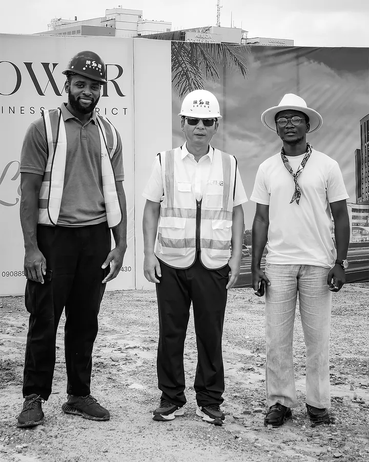 Chimezie Ikenga standing with two men in hard hats and safety vests in front of the Tri-Tower site hoarding